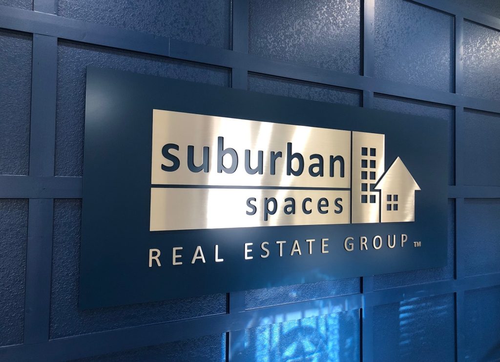 Suburban Spaces Real Estate Group sign on blue wall.